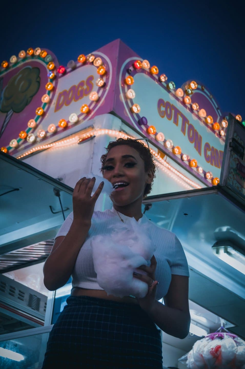 Femme mangeant un gros nuage de barbe à papa blanche à la fête foraine.