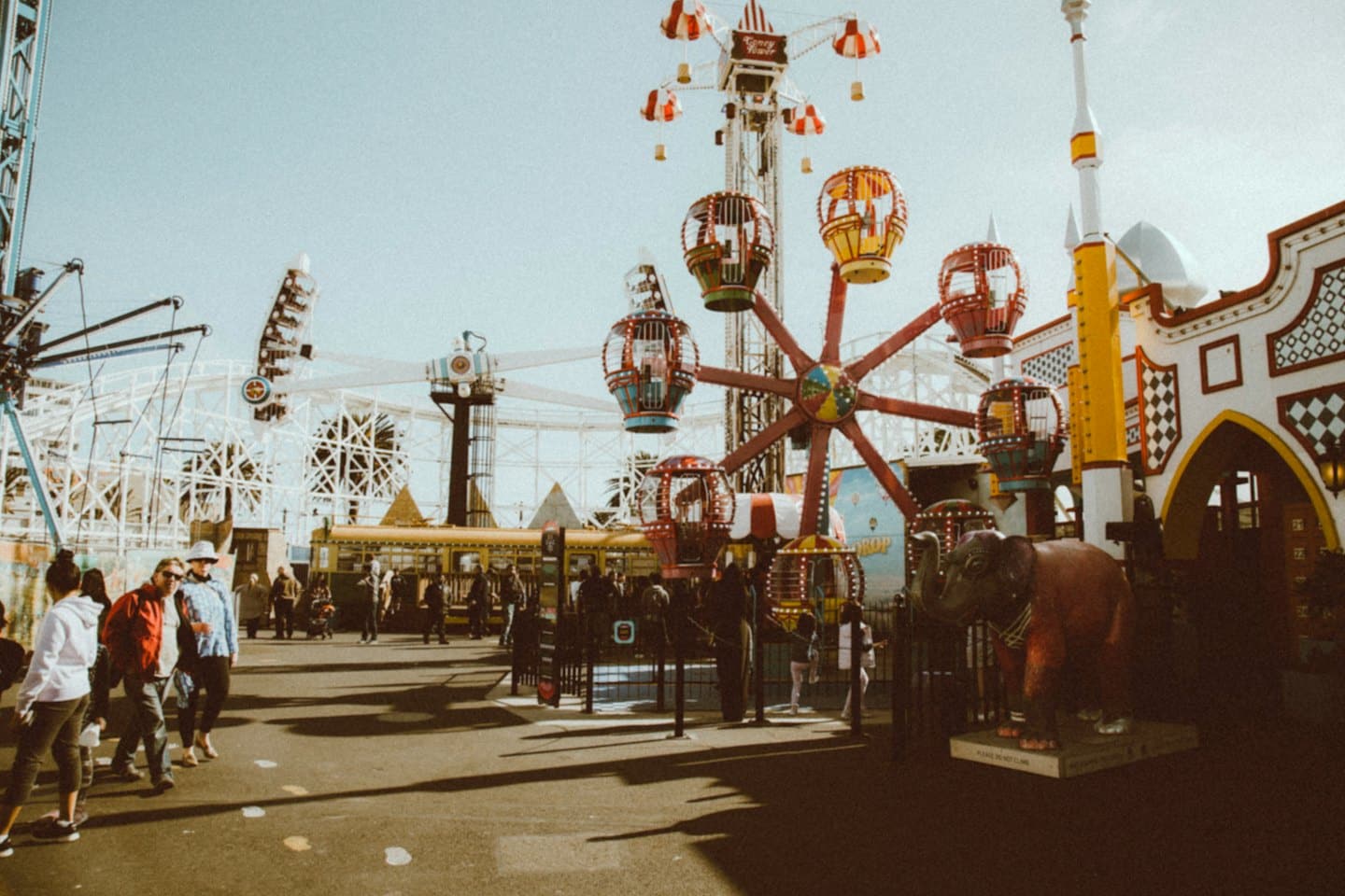 Des visiteurs passent devant des manèges de fête foraine et une statue d'éléphant rouge.