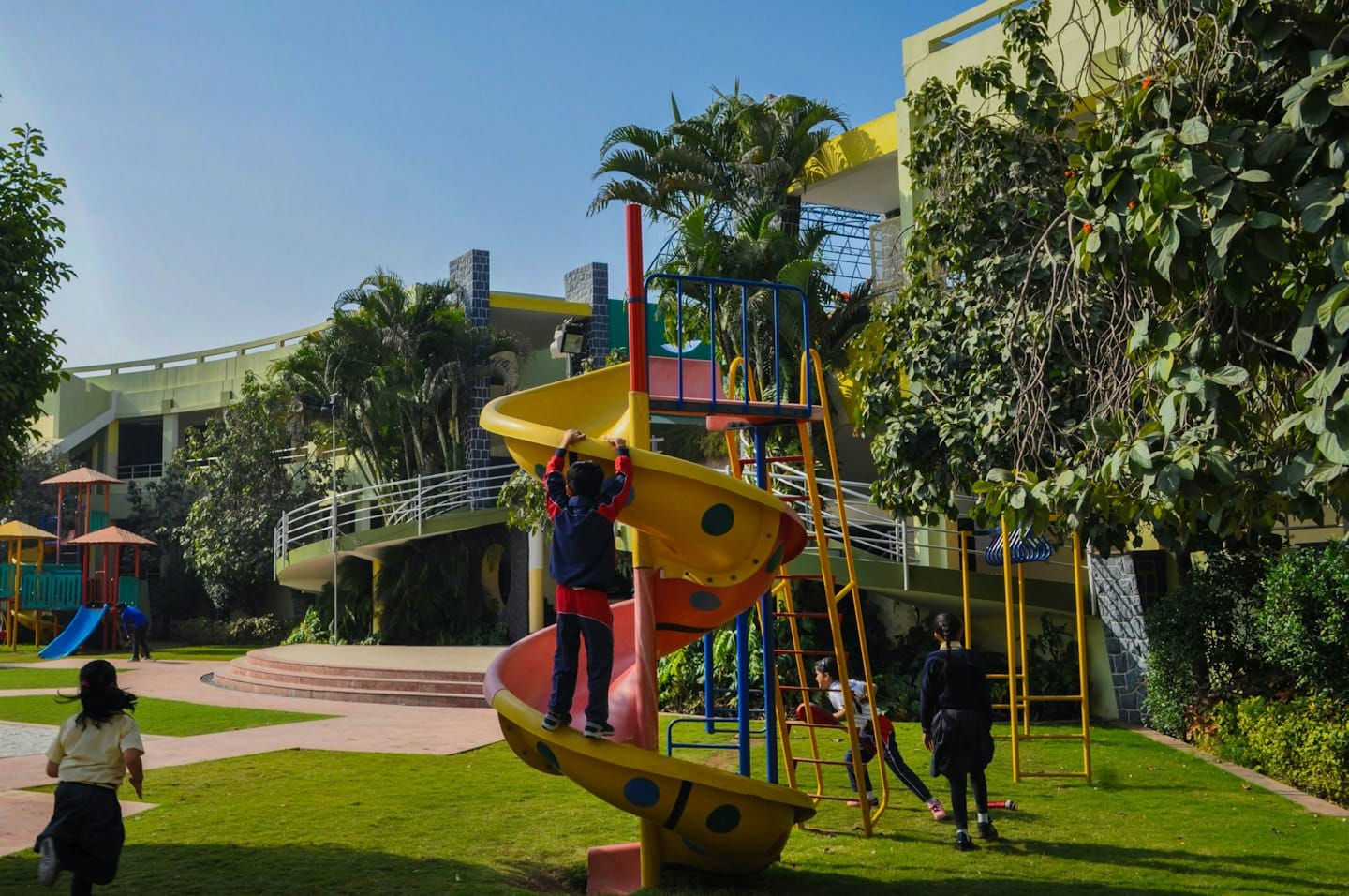 Des enfants jouent sur une aire de jeux ensoleillée avec un toboggan et des structures d'escalade.