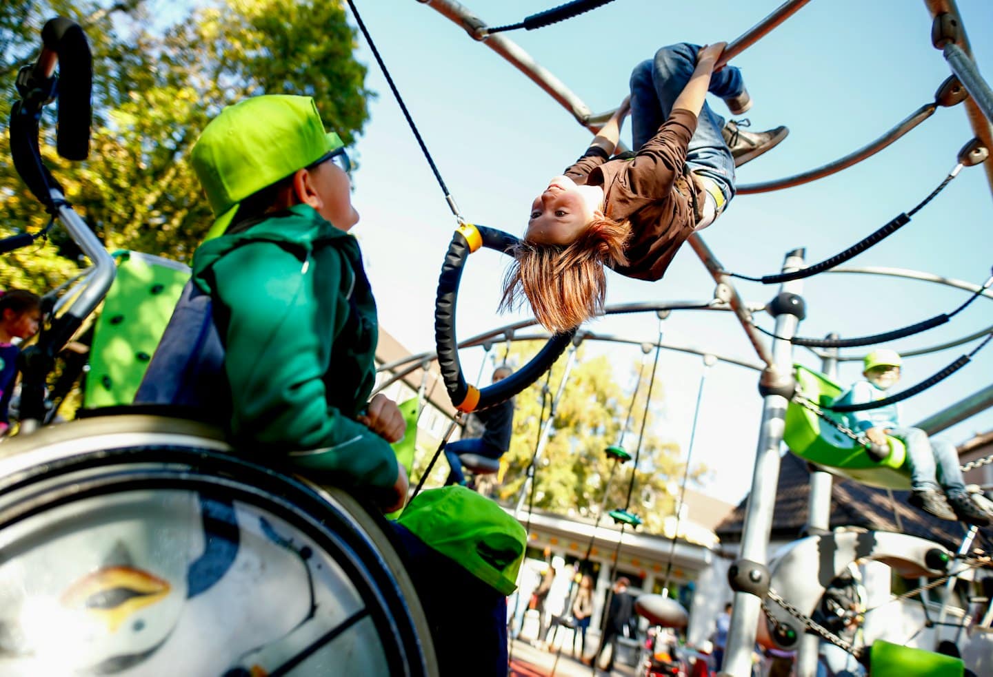 Enfant en fauteuil roulant regarde son ami qui est à l'envers sur l'aire de jeux.