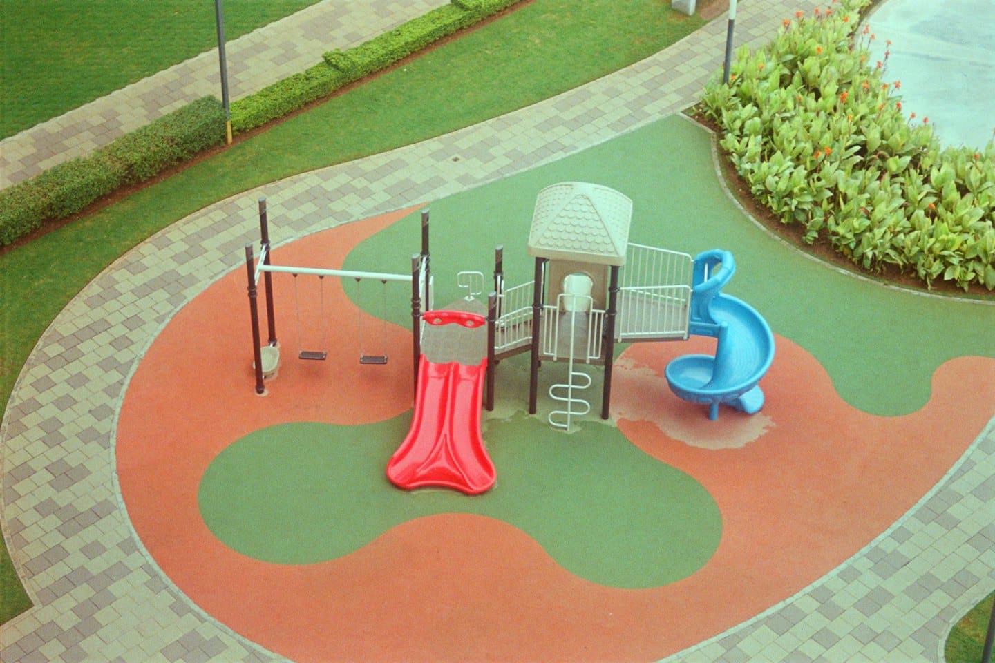Aire de jeux colorée pour enfants avec toboggans et balançoires sur de l'herbe verte.
